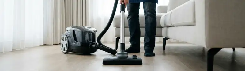 Professional house cleaner vacuuming a living room floor with a canister vacuum cleaner, Rockford, IL.