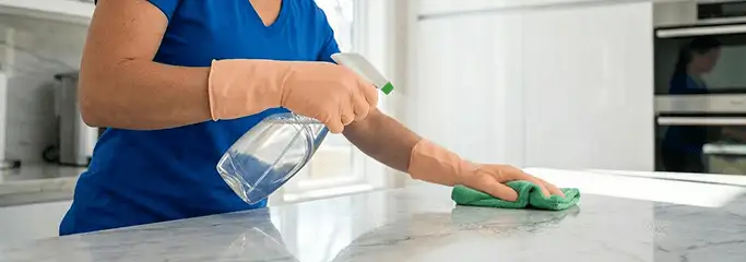 Maid service worker spraying and wiping a kitchen countertop with a microfiber cloth for sanitizing, Rockford, IL.