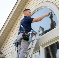 Professional window cleaner on a ladder using a squeegee to clean an exterior arched window, Rockford, IL.