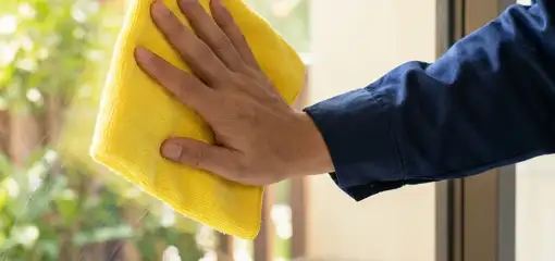 House cleaner wiping a glass window with a yellow microfiber cloth for streak-free cleaning, Rockford, IL.